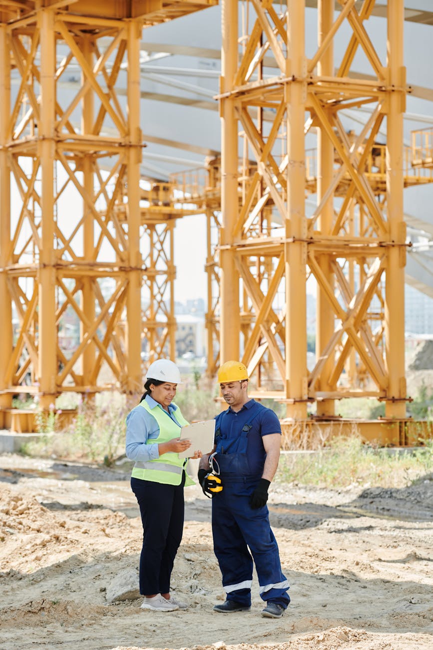 Project engineer reviewing building plans at construction site with steel framework behind